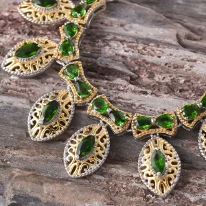 Indian tribal jewelry made of silver and gold, featuring green gemstones and photographed against a wooden backdrop.